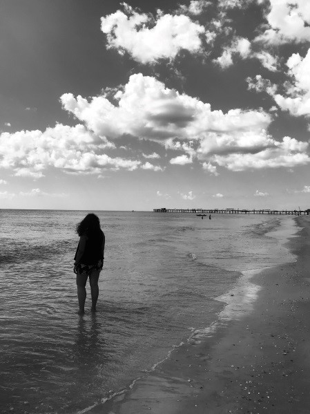Black and white photo of Aniska with her feet in the water at the beach.